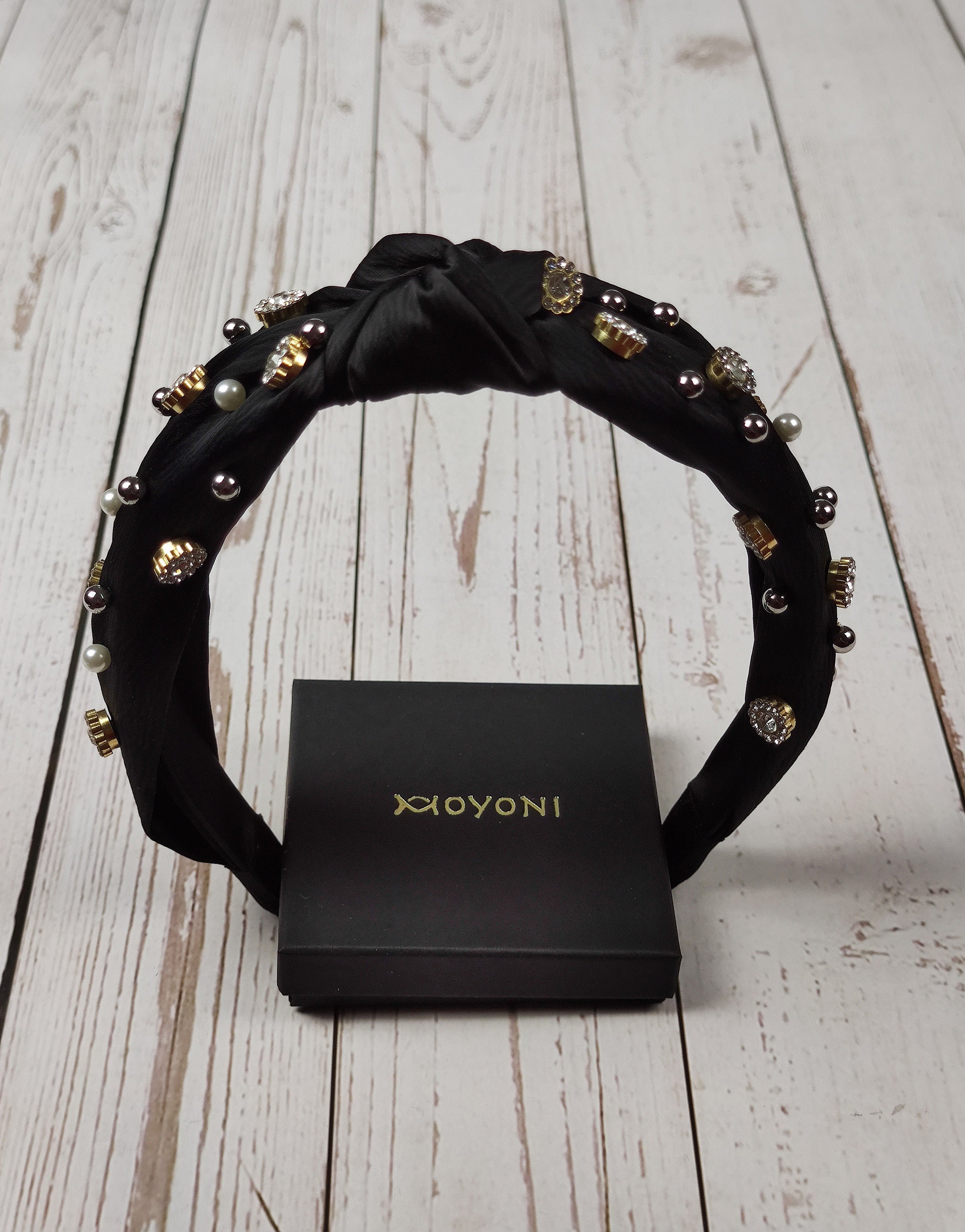 Add a touch of glamour to any outfit with this unique black satin headband, featuring gemstones and pearls.