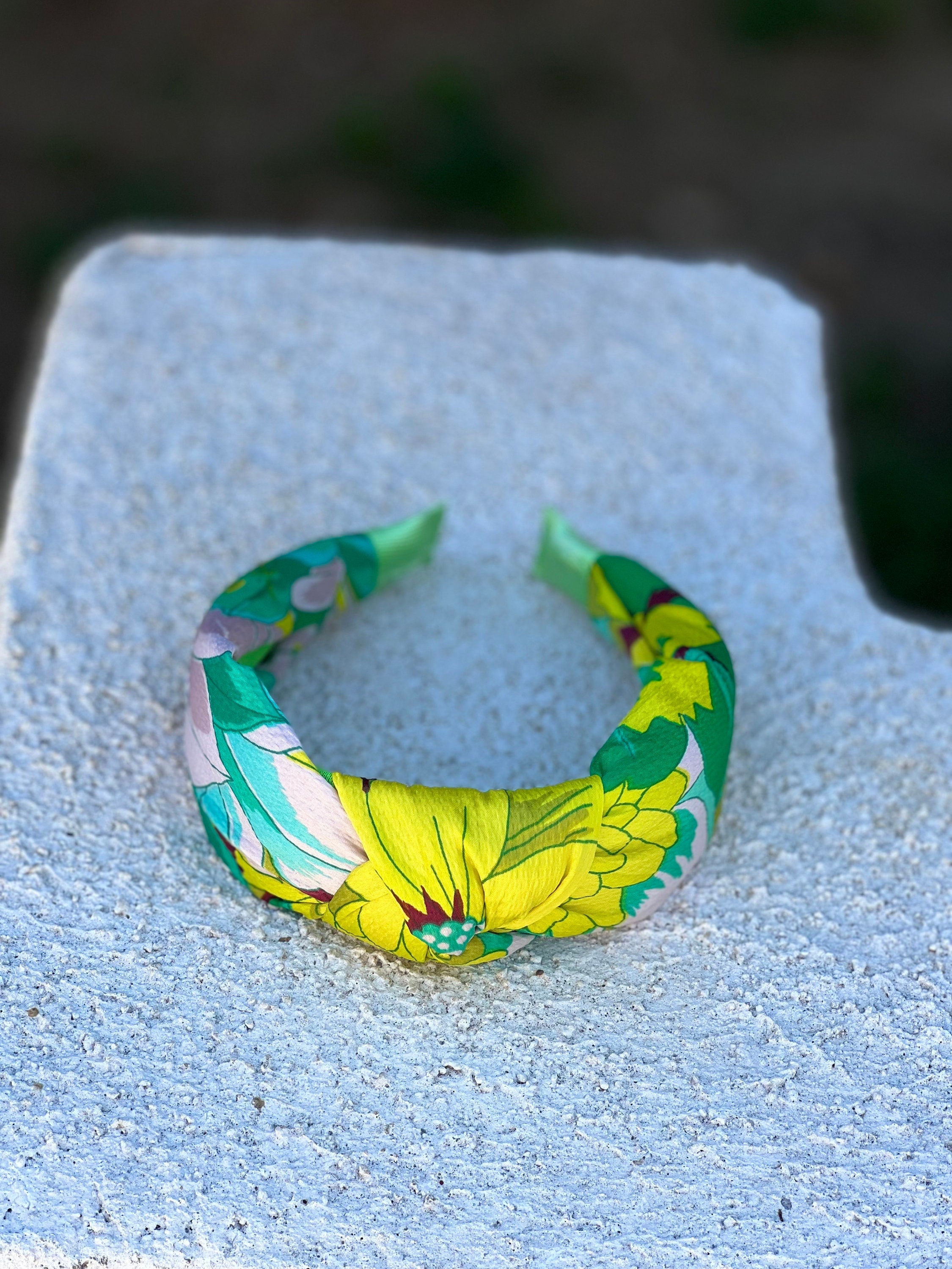 A playful flat lay of the green and yellow flower pattern knotted headband, styled with other colorful accessories and beauty products.