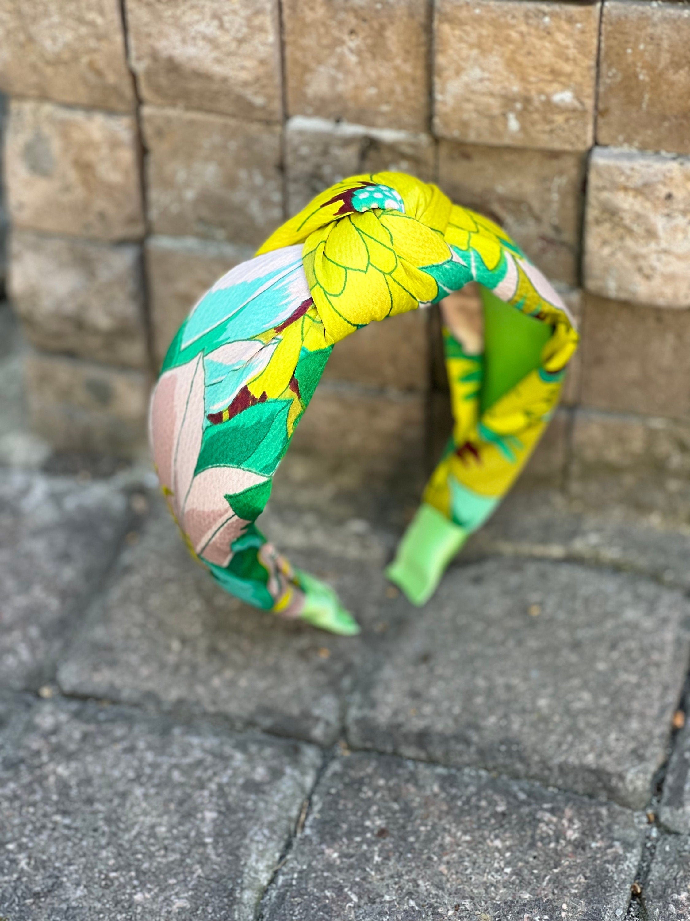 A woman wearing the green and yellow flower pattern knotted headband, styled with loose curls and a white blouse.