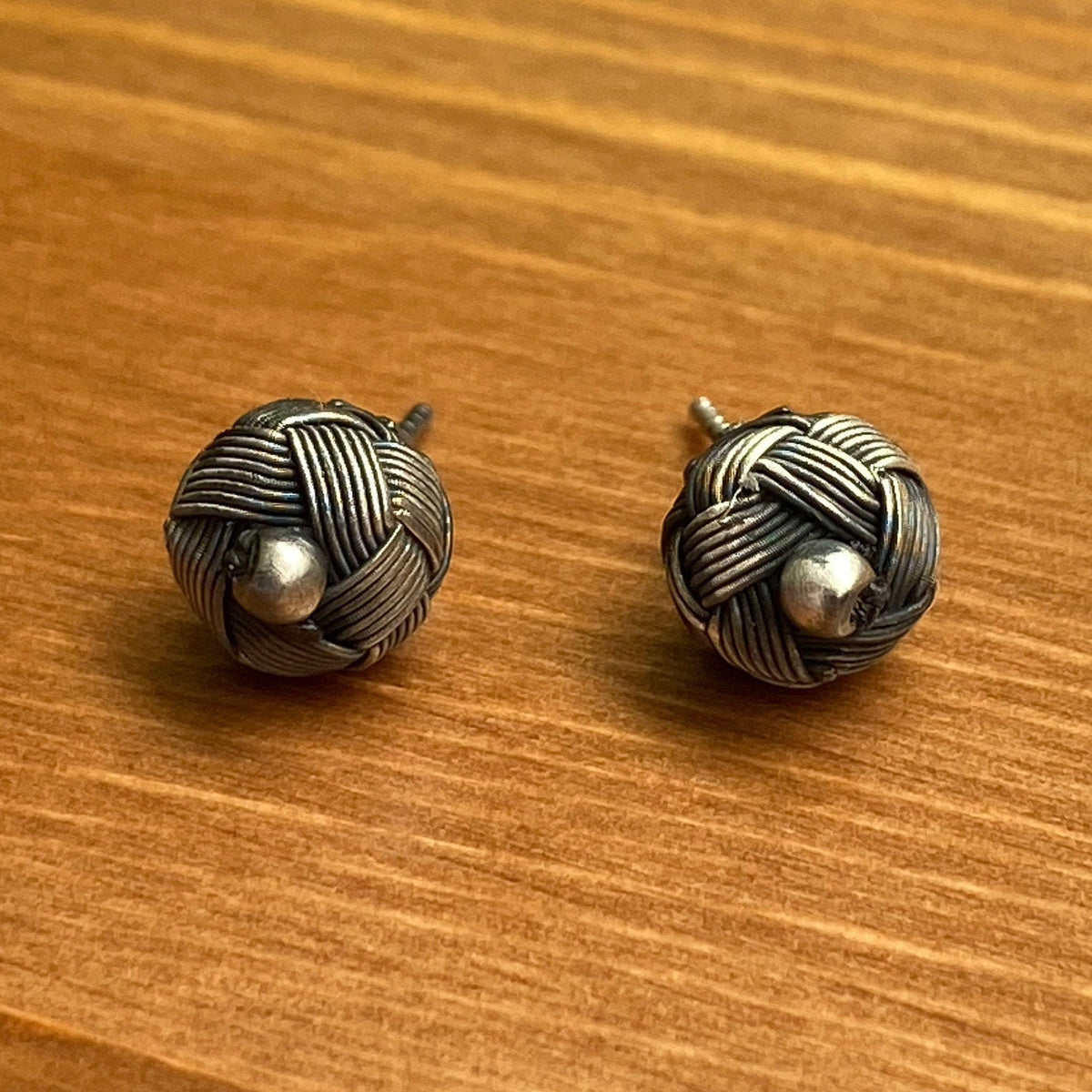 A pair of Handmade Braided Earrings in Earthy Tones displayed against a natural wooden background, highlighting their organic-inspired design.