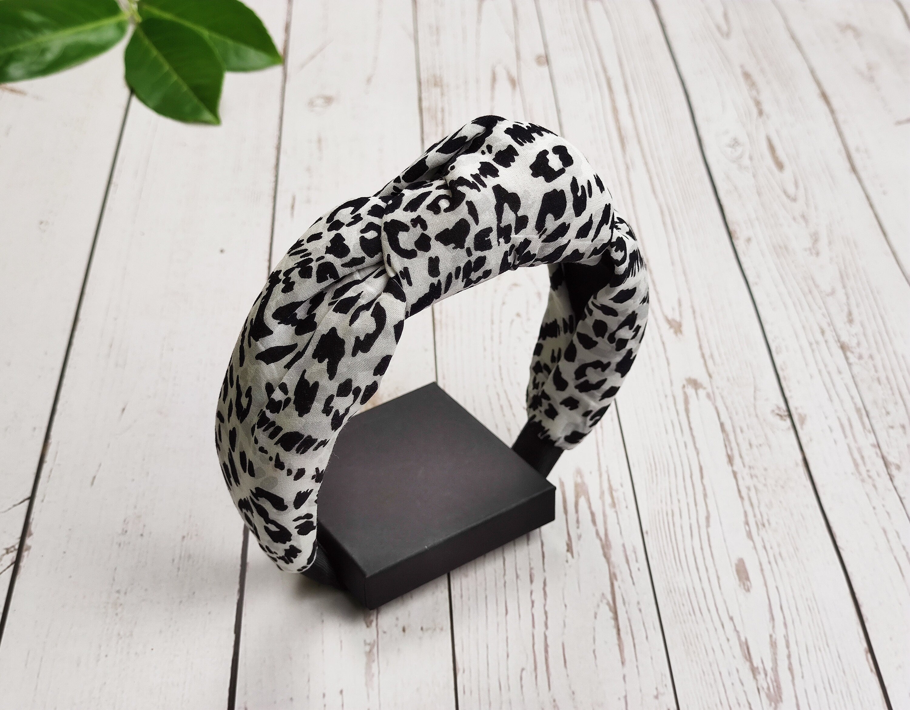 Add a touch of wild style to any outfit with this leopard print knotted headband in white, gray, and black.