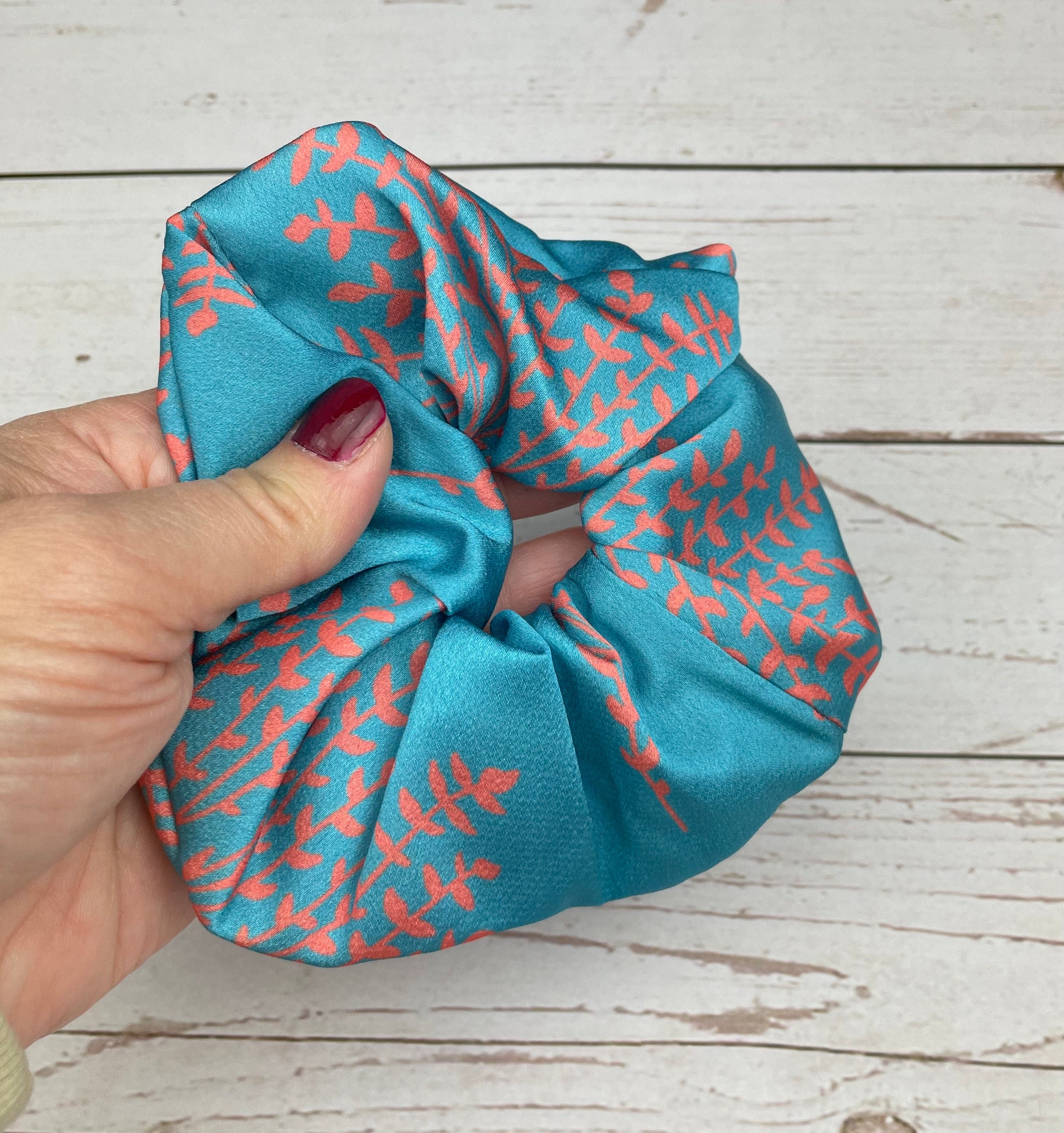 Make your hairstyle stand out with this handmade scrunchie, featuring a bold pink, blue, and green leaf pattern and a cute bow.