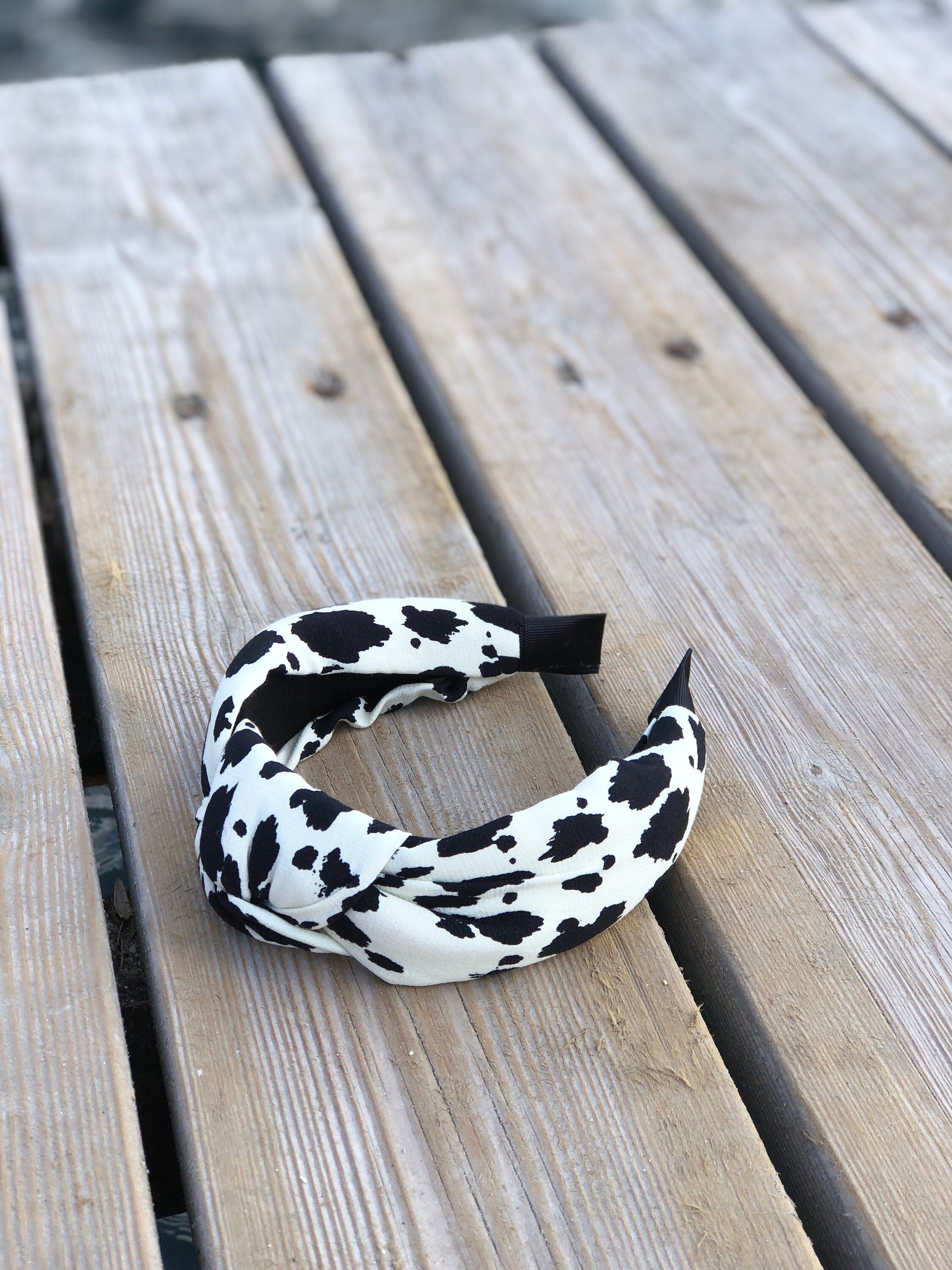 Make a statement with this unique and eye-catching white leopard headband, featuring a stylish black and white spotted print and a bow accent.